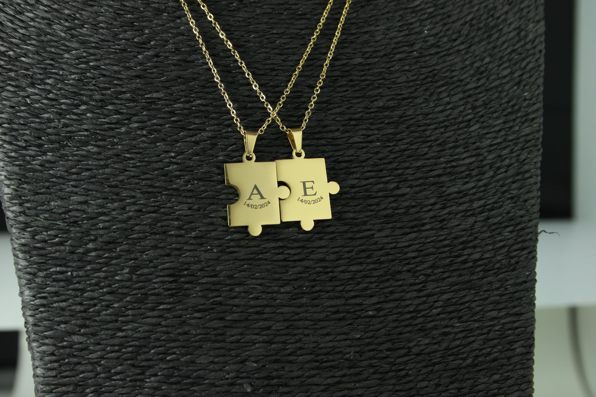 Gold puzzle piece necklaces on a textured black surface