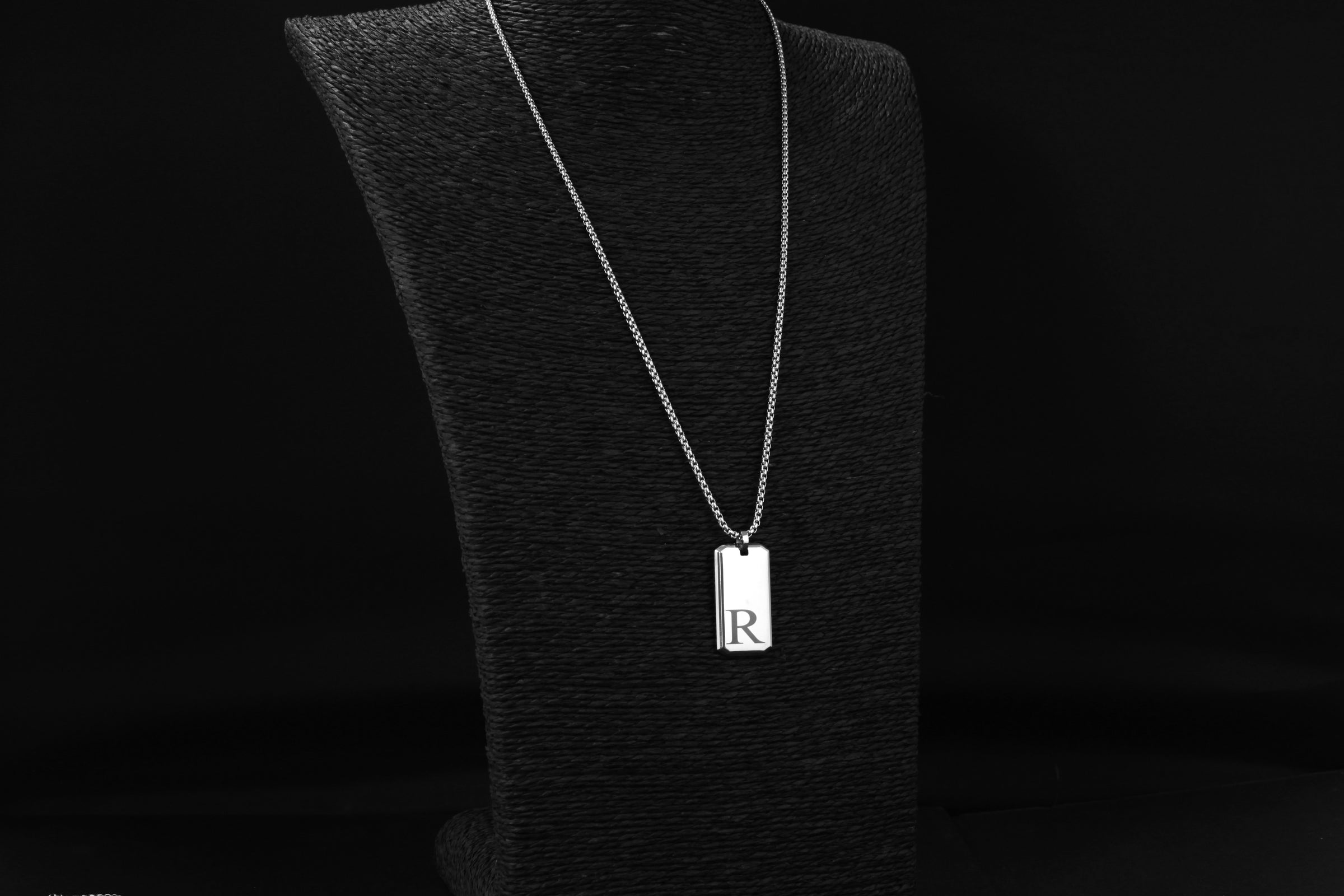 Silver necklace with a rectangular pendant on a black stand