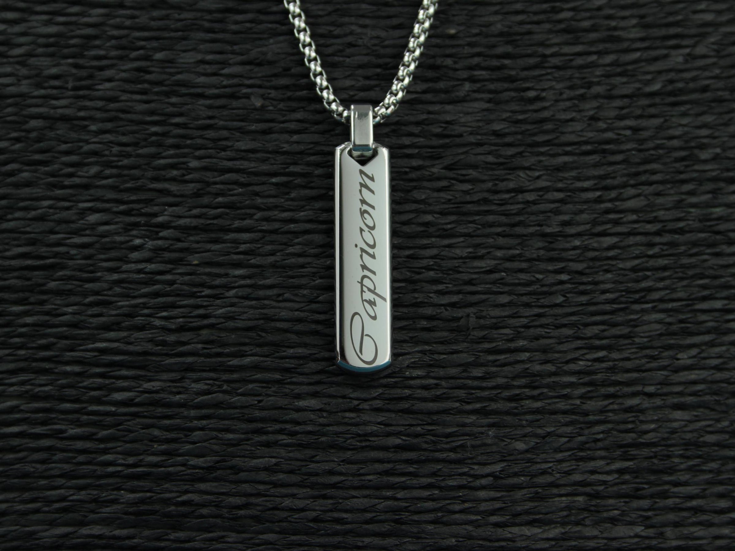 Silver pendant with 'Capricorn' engraving on a black textured background