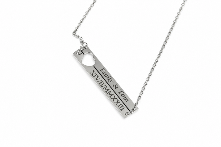 A silver bar necklace with a heart-shaped cutout and engraved personalization reading &