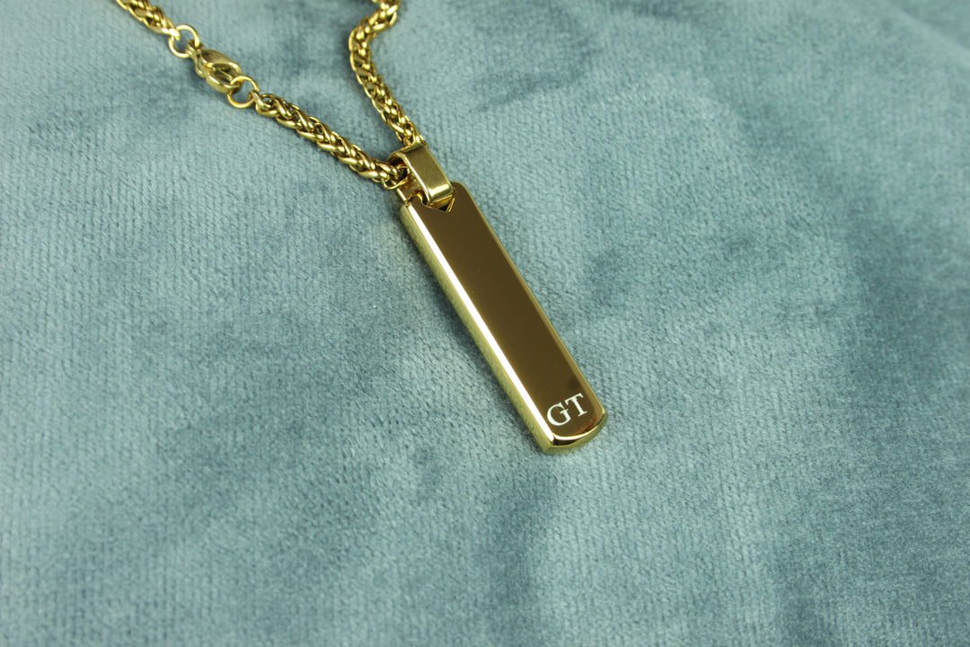 Gold necklace with a rectangular pendant on a green velvet background