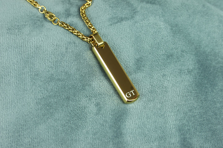 Gold necklace with a rectangular pendant on a green velvet background