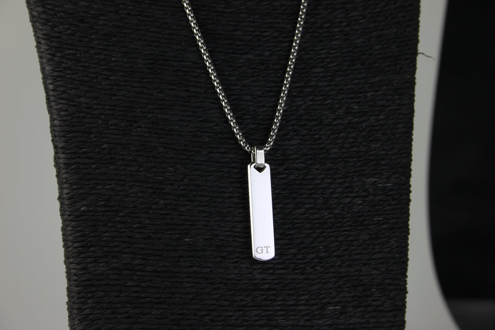 Silver necklace with a rectangular pendant on a textured black surface