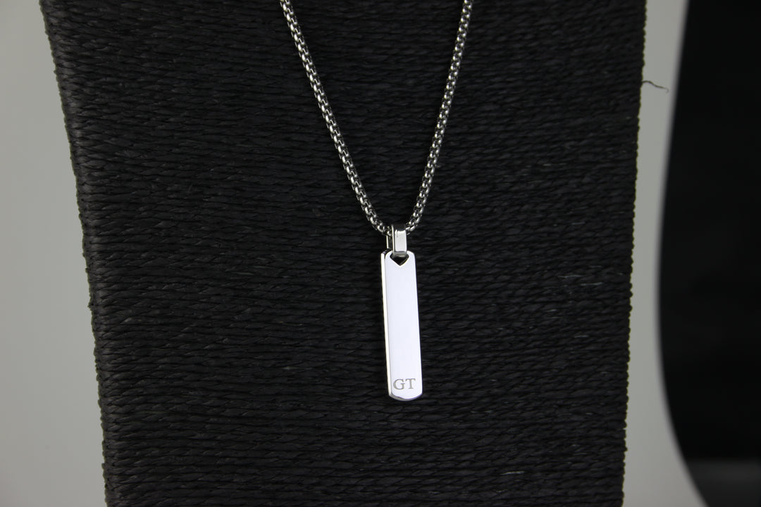 Silver necklace with a rectangular pendant on a textured black surface