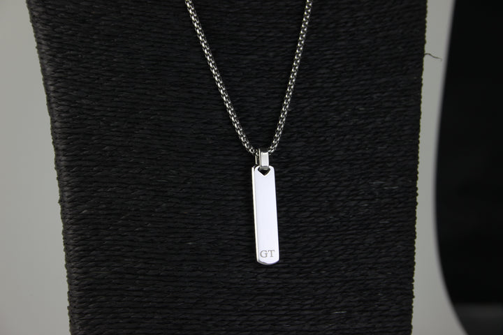 Silver necklace with a rectangular pendant on a textured black surface