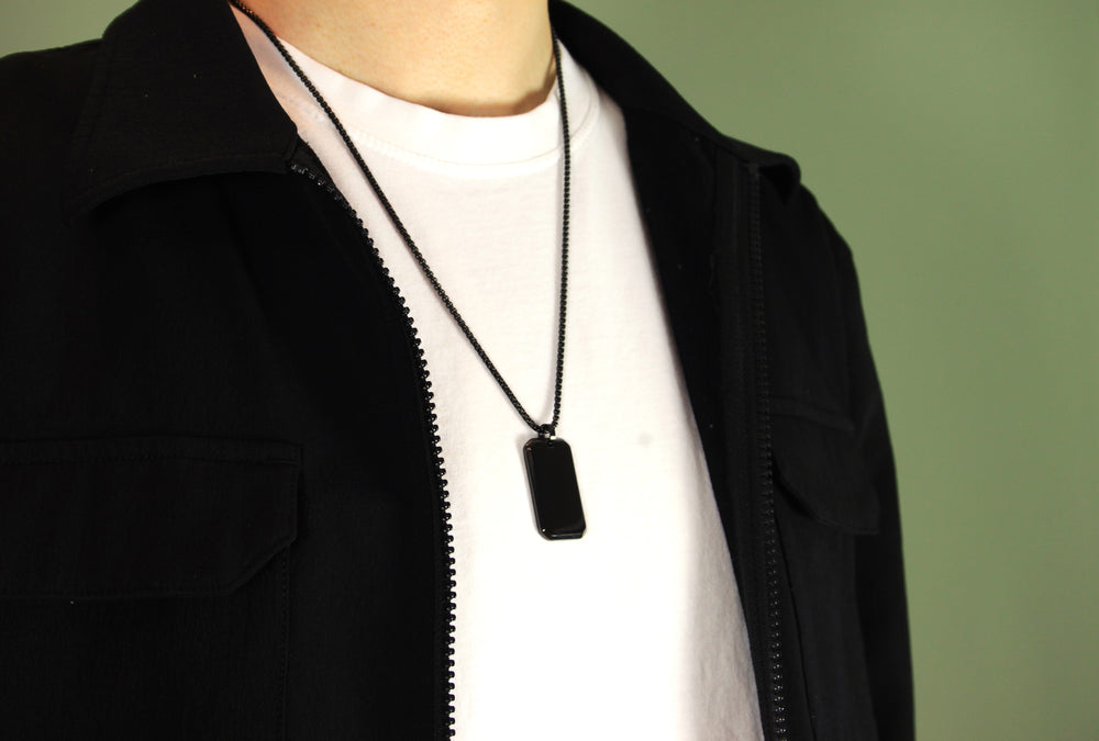 Person wearing a black dog tag necklace on a plain background