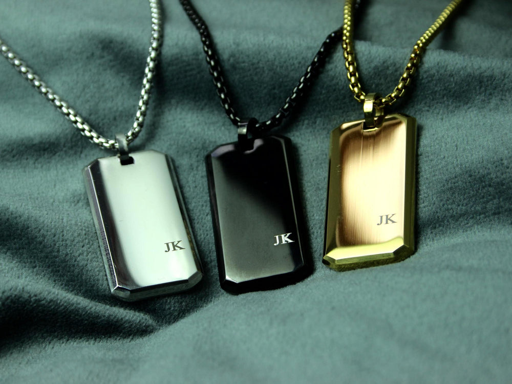 Three dog tags in silver, black, and gold on a green fabric background