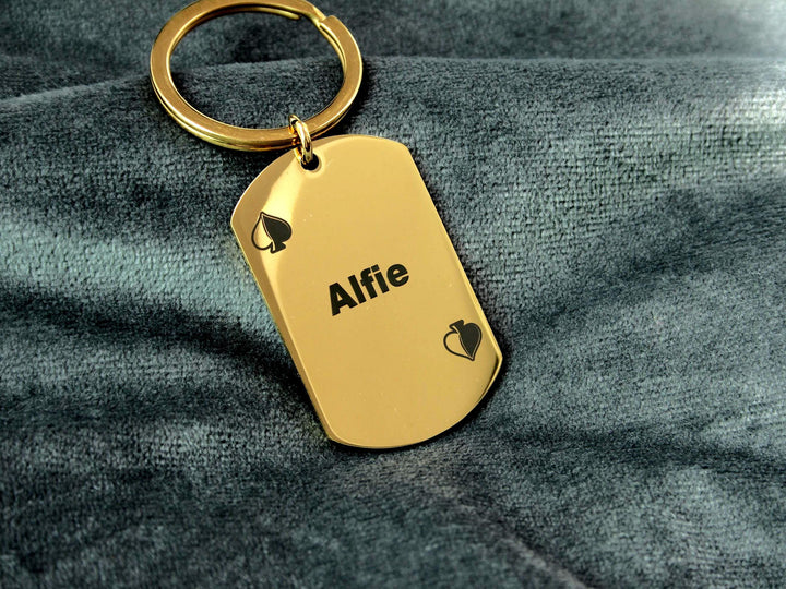 Gold keychain with 'Alfie' engraved on a gray fabric background