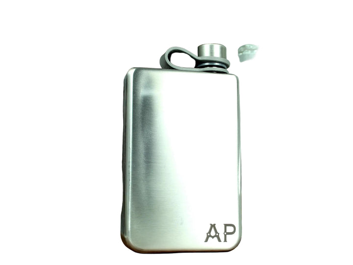 Silver flask with wooden base and glass decanter on a white surface