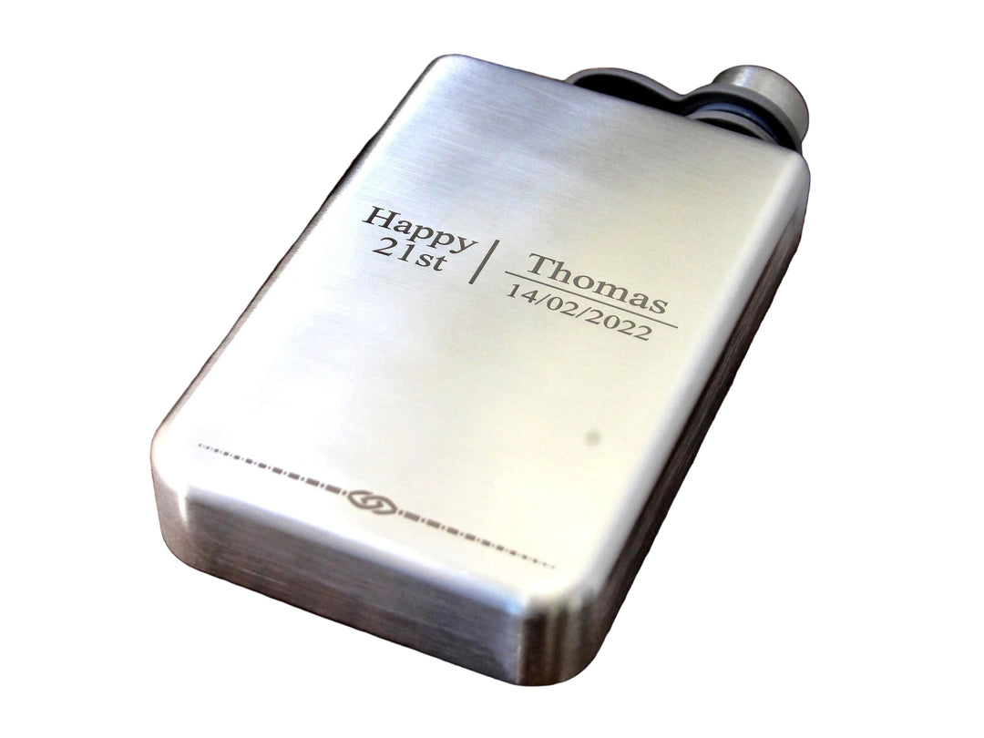 Silver flask with engraved text on a wooden surface